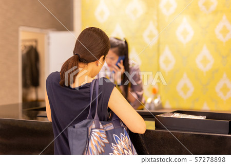 Woman at checkout in clothing store with staff on the phone enquiry. Woman at checkout in clothing store with staff on the phone enquiry. 57278898