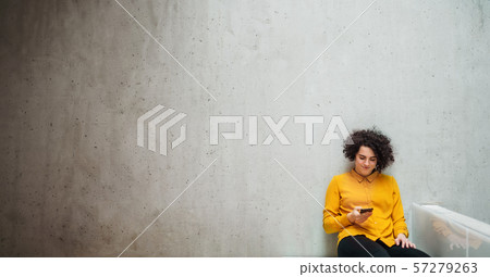 Young student or businesswoman with smartphone sitting on desk in room in a library or office. Young student or businesswoman with smartphone sitting on desk in room in a library or office. 57279263