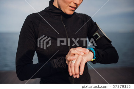 A young sportswoman standing outdoors on beach, using smartwatch. A young sportswoman standing outdoors on beach, using smartwatch. 57279335