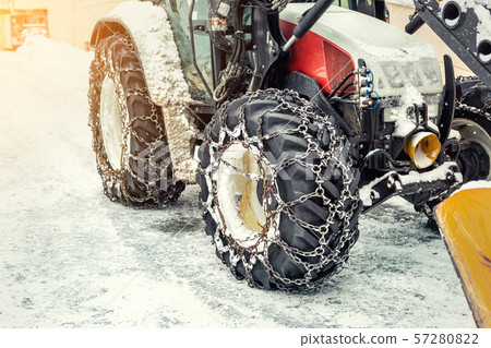 Big tractor machine with steel metal chains driving through slippery icy road or city street at 57280822