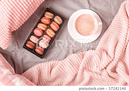 Bed with pink knitted plaid, coffee and macaroons. 57282148