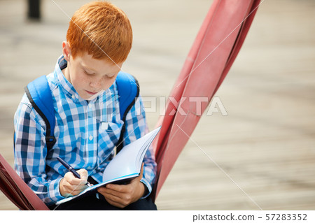 Schoolboy doing homework outdoors 57283352