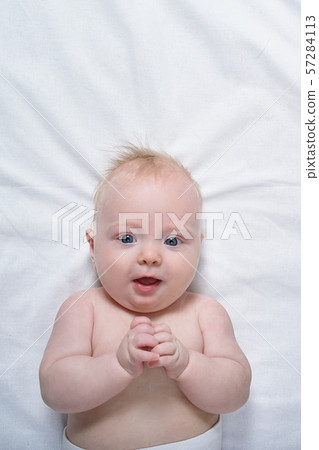 Portrait of a cute blond baby on a white sheet. Portrait of a cute blond baby on a white sheet. 57284113