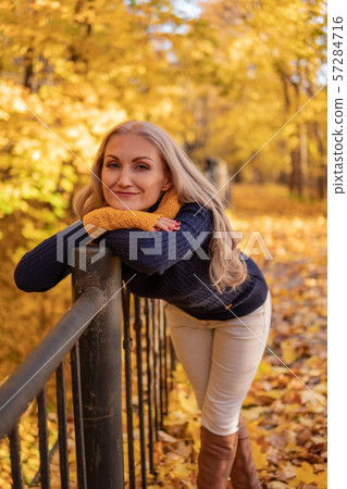 In the forest in autumn, a girl stands and looks sad on a bridge in a yellow scarf and on yellow In the forest in autumn, a girl stands and looks sad on a bridge in a yellow scarf and on yellow 57284716
