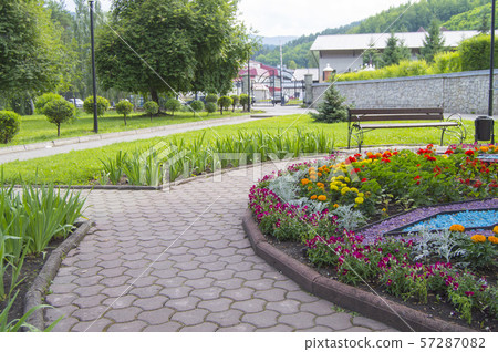 Round flower bed with colorful decorative flowers and plants, garden bench stands on the paving 57287082