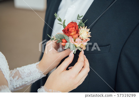 Hands of bride outdoors. Bride corrects boutonniere on groom's wedding jacket 57319299
