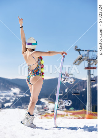 Female snowboarder in swimsuit and flower garland with snowboard on winter mountain ski resort. Female snowboarder in swimsuit and flower garland with snowboard on winter mountain ski resort. 57322324