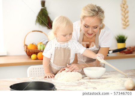 Little girl and her blonde mom in beige aprons playing and laughing while kneading the dough in Little girl and her blonde mom in beige aprons playing and laughing while kneading the dough in 57346703