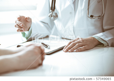 Doctor and female patient sitting at the desk and talking in clinic near window. Medicine and health 57349065