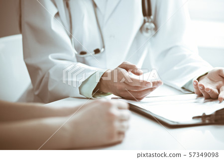 Doctor and female patient sitting at the desk and talking in clinic near window. Medicine and health 57349098