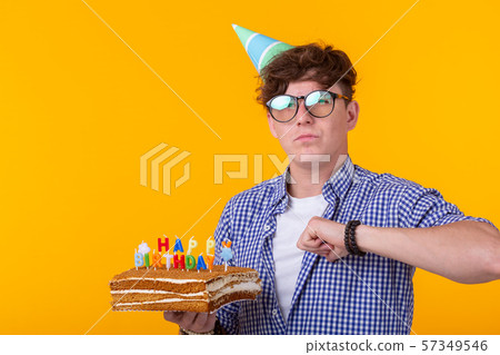 Portrait of a funny positive guy with a paper cap and glasses holding a congratulatory cake in his 57349546