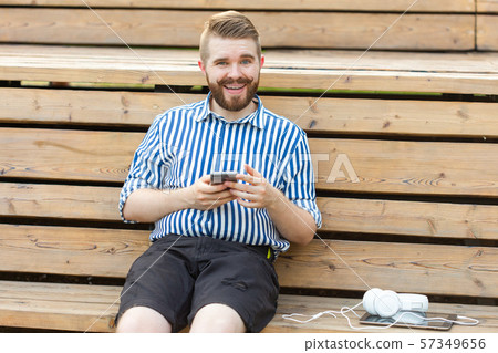 Happy young male hipster student with a mustache and beard writing sms message to his friends Happy young male hipster student with a mustache and beard writing sms message to his friends 57349656