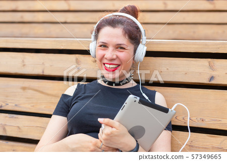 Beautiful young female student is studying using a tablet and headphones while sitting in a park on Beautiful young female student is studying using a tablet and headphones while sitting in a park on 57349665