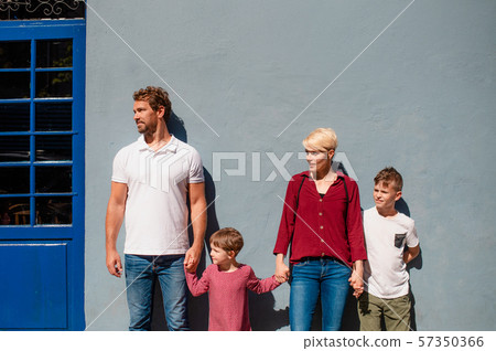 Front view of young family with two small children standing outdoors in town. 57350366