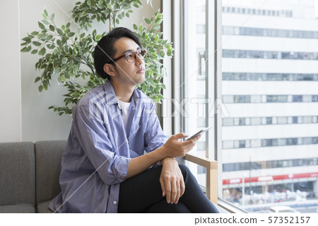 Man looking out of window with smartphone in hand 57352157