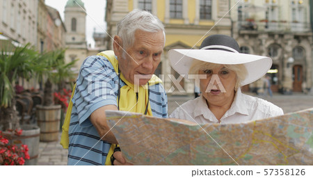 Senior male and female tourists standing with a map in hands looking for route 57358126