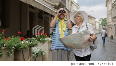 Senior male and female tourists standing with a map in hands looking for route 57358193
