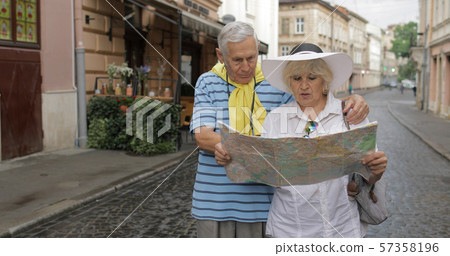 Senior male and female tourists standing with a map in hands looking for route 57358196