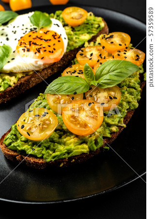 Open sandwiches with avocado guacamole, yellow cherry tomatoes, fried egg and basil on a black plate Open sandwiches with avocado guacamole, yellow cherry tomatoes, fried egg and basil on a black plate 57359589