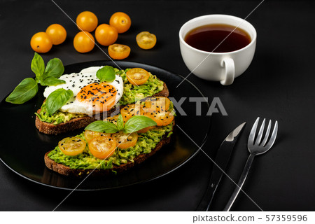 Open sandwiches with avocado guacamole, yellow cherry tomatoes, fried egg and basil on a black plate Open sandwiches with avocado guacamole, yellow cherry tomatoes, fried egg and basil on a black plate 57359596