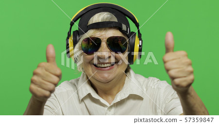 Elderly woman listens to music in headphones. Thumb up. Grandmother. Chroma key 57359847