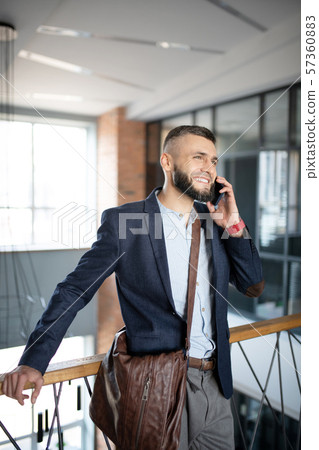 Businessman wearing brown hand bag speaking by phone Businessman wearing brown hand bag speaking by phone 57360883