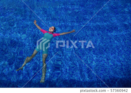 Child girl in goggles, swimsuit and cap relaxes on back in swimming pool. Child girl in goggles, swimsuit and cap relaxes on back in swimming pool. 57360942