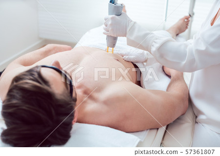 Cosmetologist using laser to remove chest hair of man 57361807