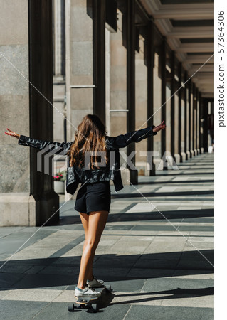 Beautiful young skater woman riding on her longboard in the city. Stylish girl in street clothes Beautiful young skater woman riding on her longboard in the city. Stylish girl in street clothes 57364306