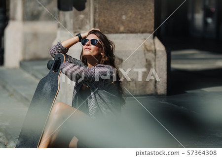 Portrait of Beautiful young woman sitting on the ground and holding a longboard in the city street Portrait of Beautiful young woman sitting on the ground and holding a longboard in the city street 57364308