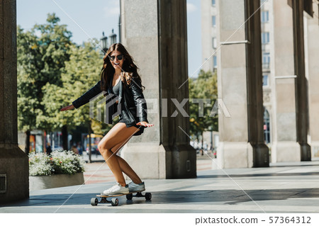 Beautiful young skater woman riding on her longboard in the city. Stylish girl in street clothes Beautiful young skater woman riding on her longboard in the city. Stylish girl in street clothes 57364312