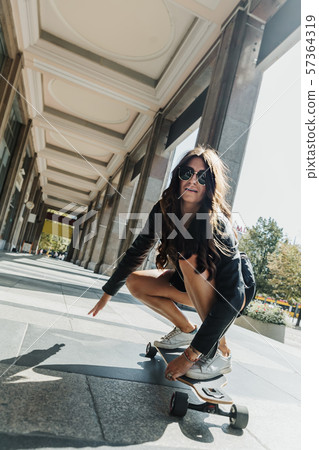 Beautiful young skater woman riding on her longboard in the city. Stylish girl in street clothes Beautiful young skater woman riding on her longboard in the city. Stylish girl in street clothes 57364319