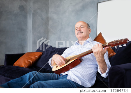 Senior hispanic man at home learning to play guitar. 57364784