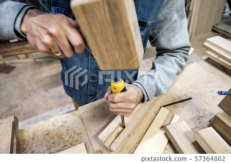 carpenter makes a hole in the wooden furniture detail with a hammer and chisel. 57364802