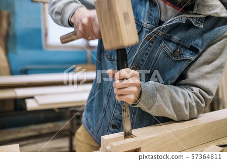 carpenter makes a hole in the wooden furniture detail with a hammer and chisel. carpenter makes a hole in the wooden furniture detail with a hammer and chisel. 57364811