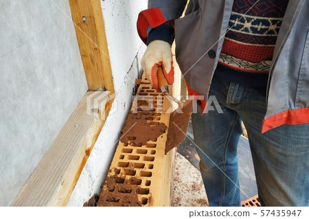 In the summer day the master builds the facade of the house made of red brick. 57435947