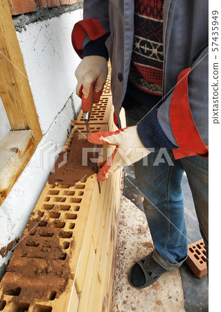 In the summer day the master builds the facade of the house made of red brick. 57435949