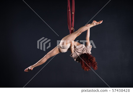 Female athletic, sexy and flexible aerial circus artist with redhead dancing in the air on the silk 57438428