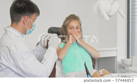 Young girl refusing showing teeth to a dentist covering her mouth with her hands Young girl refusing showing teeth to a dentist covering her mouth with her hands 57446857