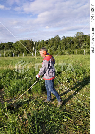 The headphone and glasses worker mows the grass in 57456807
