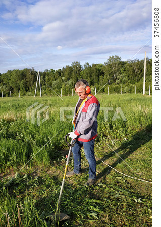 The headphone and glasses worker mows the grass in 57456808