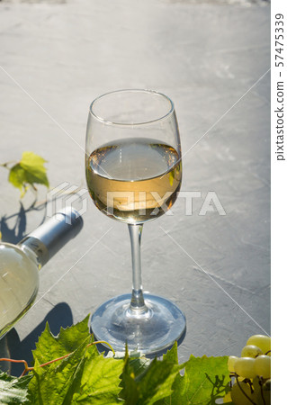 Bottle of white wine with wineglass, ripe grape on concrete grey table. 57475339