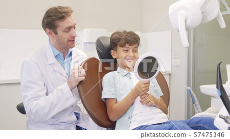 Lovely boy checking out his healthy teeth in the mirror after dental examination Lovely boy checking out his healthy teeth in the mirror after dental examination 57475346