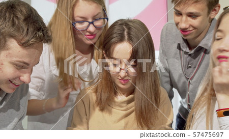 Teenage girl writing in her textbook with her classmates surrounding her Teenage girl writing in her textbook with her classmates surrounding her 57475697