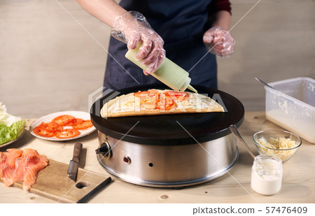 Cook pouring green sauce from bottle on pizza on portable cooktop. Ingredients for vegetarian pizza Cook pouring green sauce from bottle on pizza on portable cooktop. Ingredients for vegetarian pizza 57476409