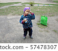 A little girl with juice in her hand stands on the street and takes a pensive look.Nearby is a bag.  57478307