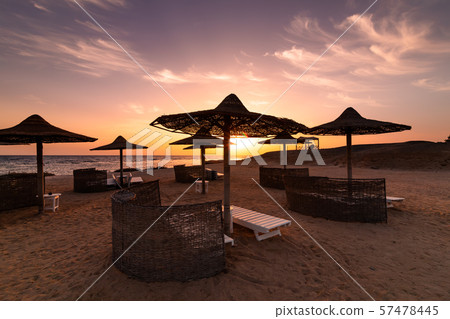 Sunset at the beach with palm trees, parasols and sunbeds. Sunset at the beach with palm trees, parasols and sunbeds. 57478445