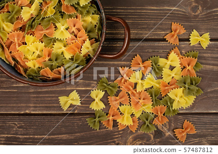 Raw farfalle tricolore on brown wood Raw farfalle tricolore on brown wood 57487812