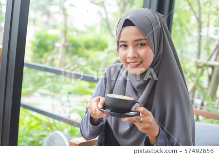 Asian muslim woman in hijab smilling with coffee in cafe morning. Asian muslim woman in hijab smilling with coffee in cafe morning. 57492656