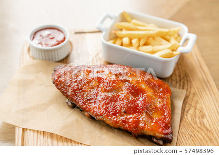 Delicious Pork ribs. Full rack of ribs BBQ on wooden plate with french fries and salad Delicious Pork ribs. Full rack of ribs BBQ on wooden plate with french fries and salad 57498396